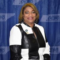 Kimberly Strong Black woman with black and white jacket smiling on front of a blue background