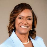Liz Appling Black woman wearing baby blue blazer and pearls smiling for camera against a beige background