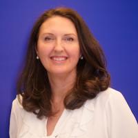 Abby Garrison Woman with dark hair and white top smiling at camera in front of a royal blue background