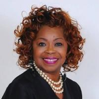 Beverly McKeldin Black woman wearing a black shirt and pearls smiling in front of a white backgrond