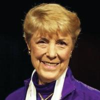 Jo Coke White woman with short blonde hair and purple blazer smiling in front of a black background
