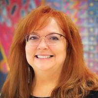 Regina McDevitt Committee Chair Red haired woman smiling in front of a patterned backgroun