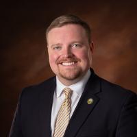 Cody Harvey White male with suit and gold tie in front of a brown background