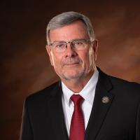Chip Henderson White male in suite and tie in front of a brown background