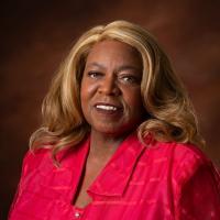 Marvene Noel BLack woman in red top with blonde hair in front of brown background
