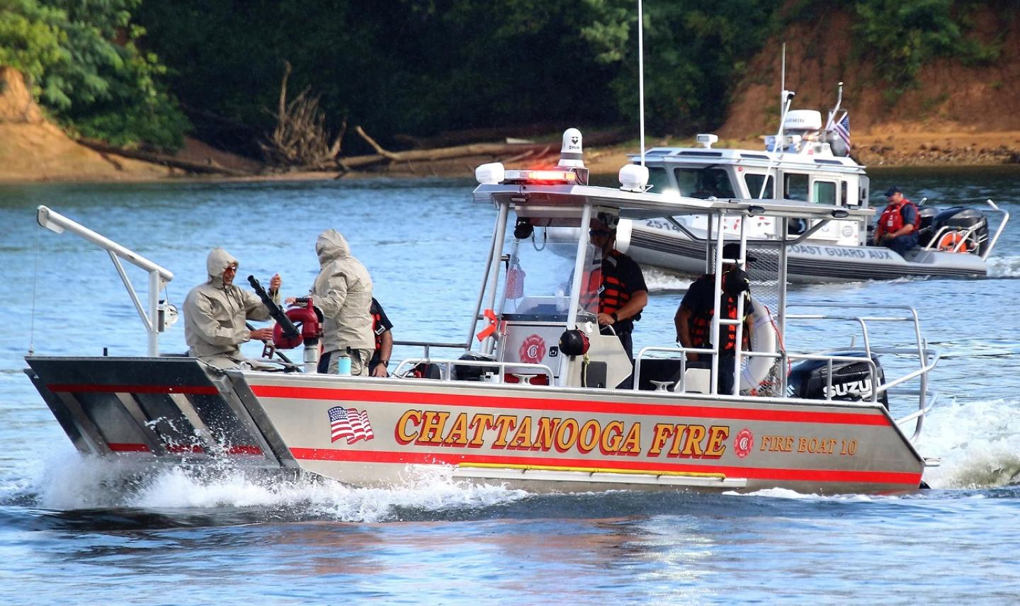 Personas en un bote en el agua, con el departamento de bomberos visible al fondo.