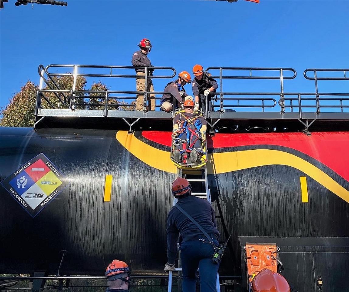 Hombres participando en un ejercicio de entrenamiento con cuerda para bomberos cerca de un tren.