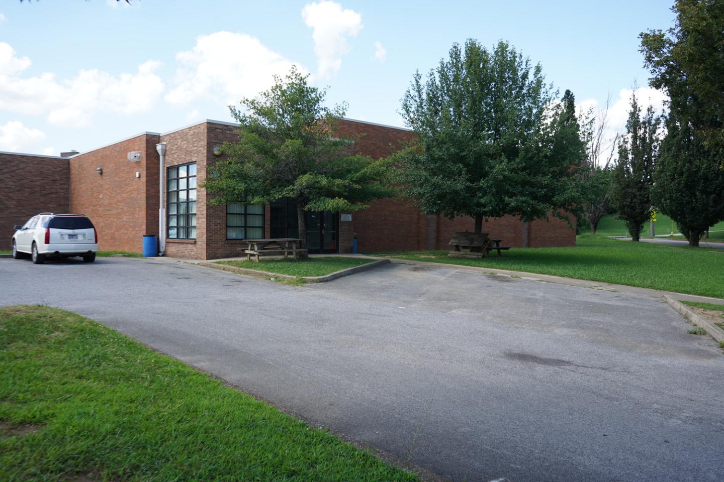 Brick building of Westside Community Center with large windows, surrounded by green trees and grass, with a white SUV parked in the driveway