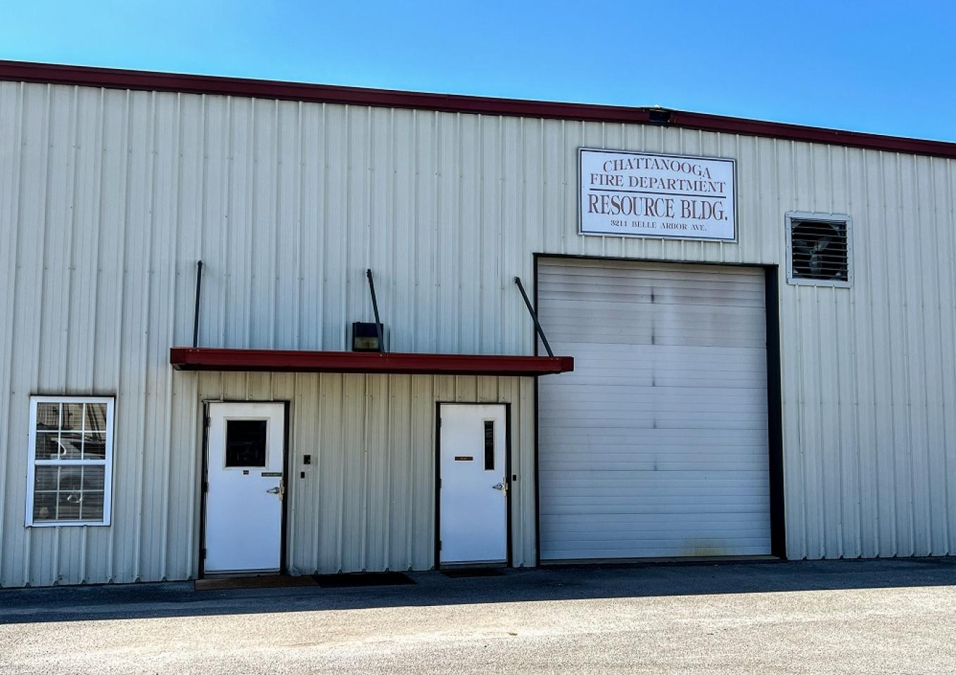 White metal building with red trim labeled 'Chattanooga Fire Department Resource Bldg.', featuring two white doors and a large garage door