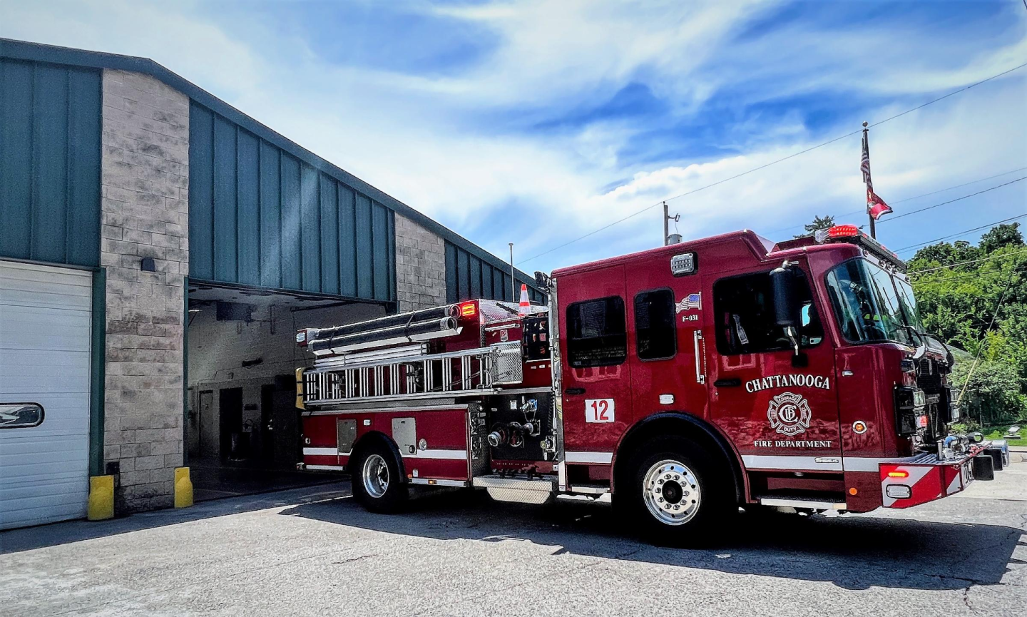  Side view of a red fire truck parked in front of building at fire station 12.