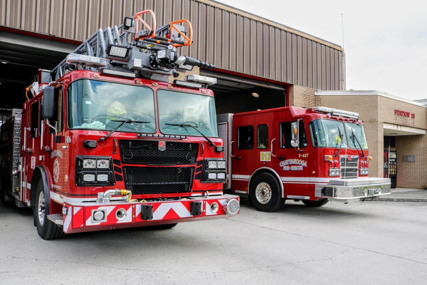 Side view of two big and bright red fire truck stationed at fire station 13.