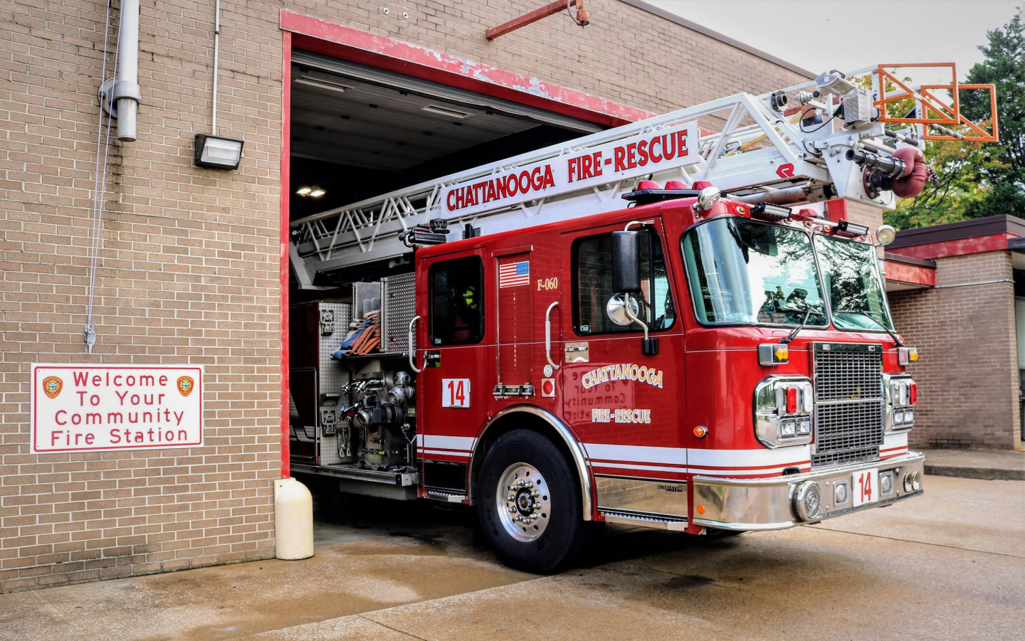 Side view of a red fire truck parked at fire station 14. The building has a sign thar reads "Welcome to your coomunity fire station"