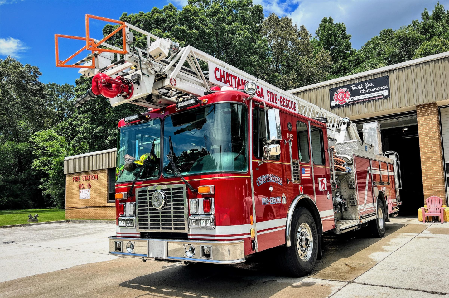 Exterior of Fire Station 16 with red brick walls, white garage doors and a bright big red fire truck parked in front of it.