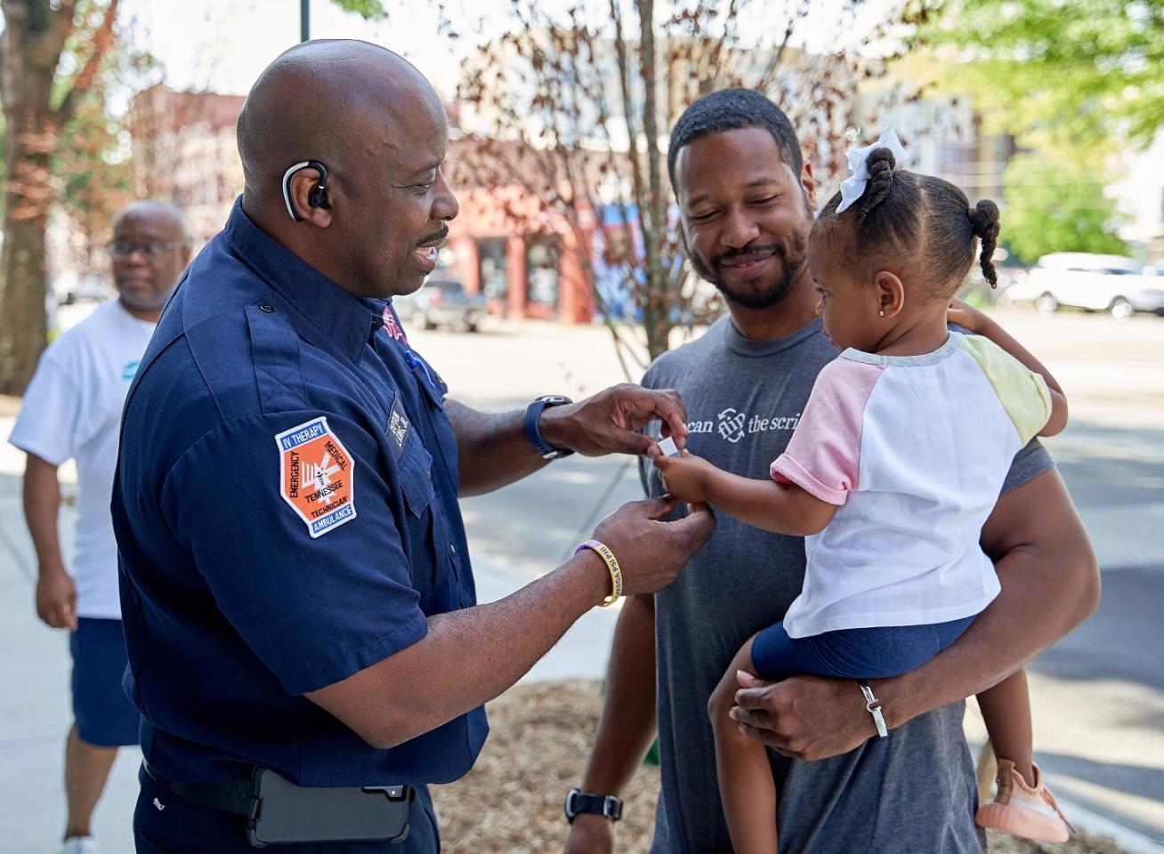 A firefighter holding the hand of a little girl carried in her father's arms