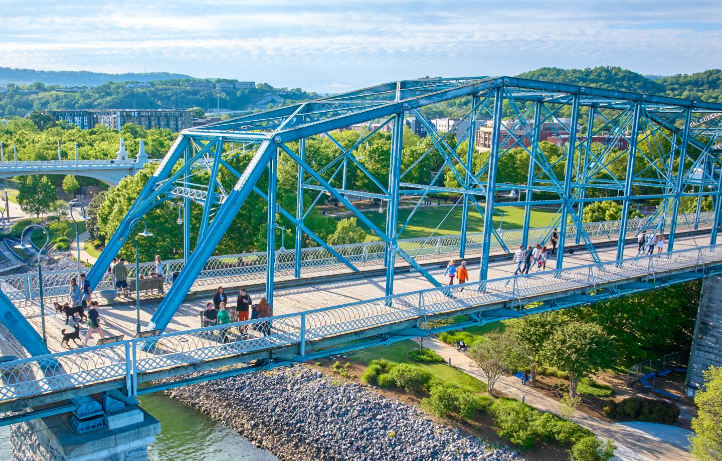 People walking on Walnut Street Bridge with scenic views of Chattanooga in the background.