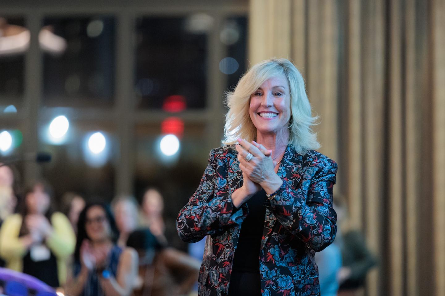 woman with blonde air and floral blazer clapping