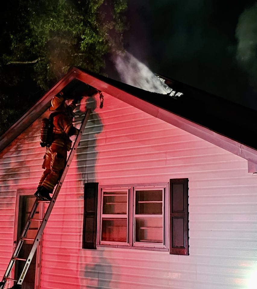 A fire fighter going up to the roof where smoke can be seen