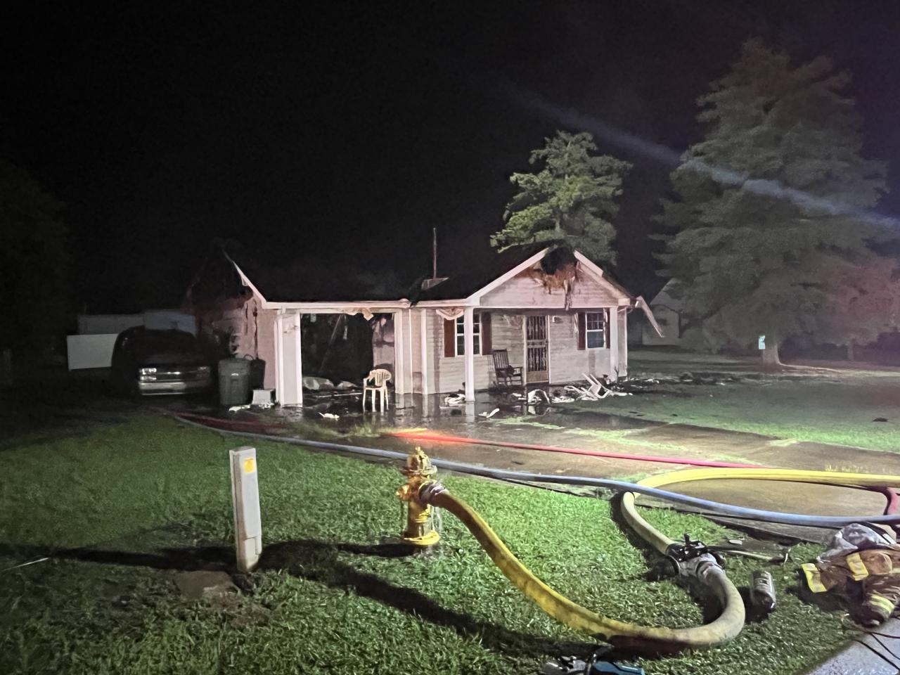 Burned house with water hoses from fire truck laying in front yard