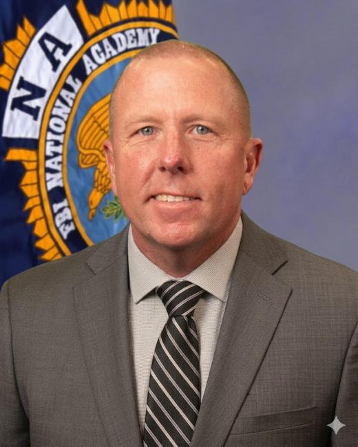 FBI Academy graduate Lieutenant Justin Kilgore in a suit in front of the FBI Nation Academy Flag