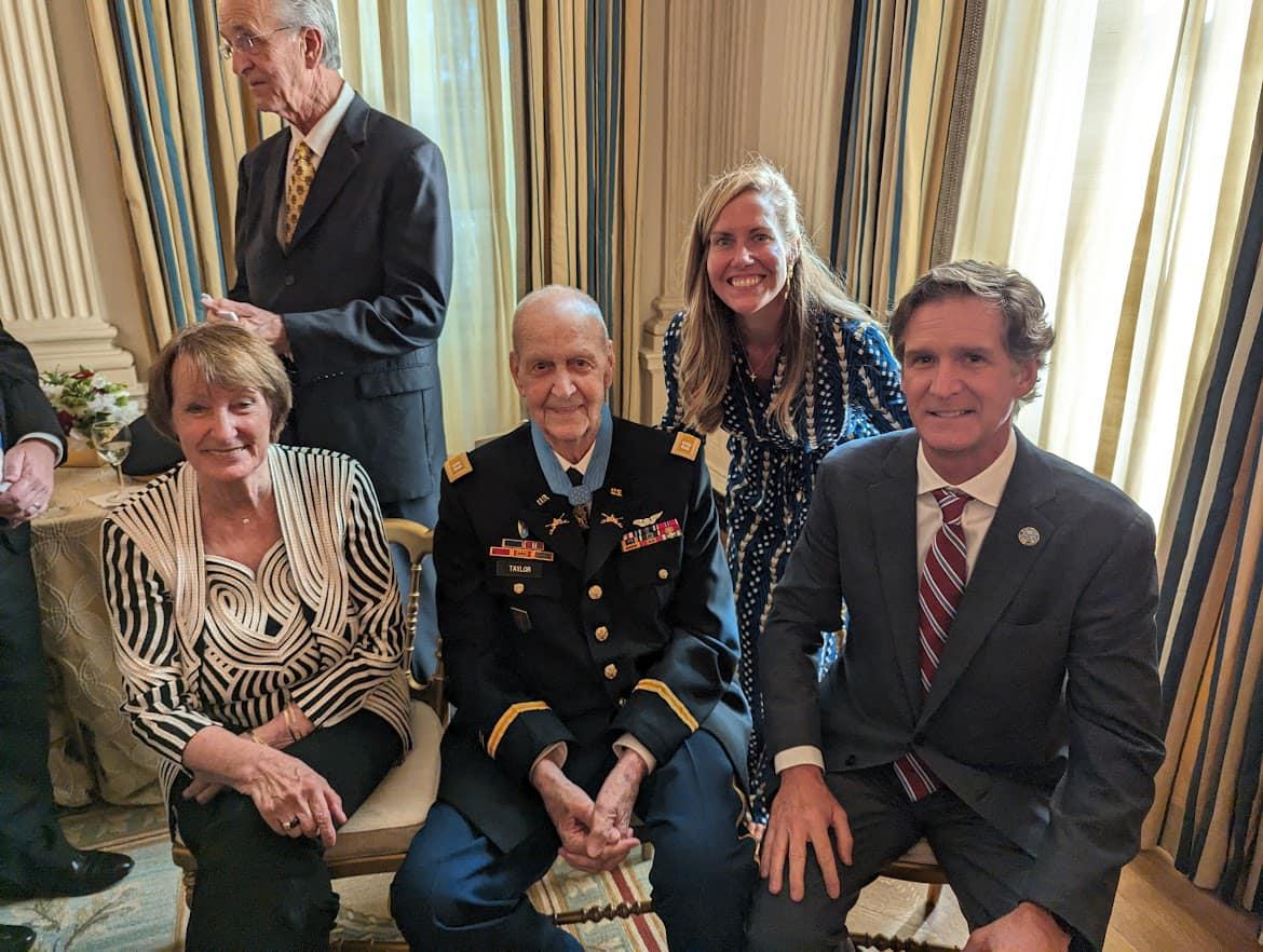 Un grupo de personas con trajes y corbatas sentados en una sala: la esposa del Capitán Taylor, Toni Taylor; el Capitán Larry Taylor; la Primera Dama de Chattanooga, Ginny Kelly; y el Alcalde Tim Kelly. Recipientes de la Medalla de Honor.