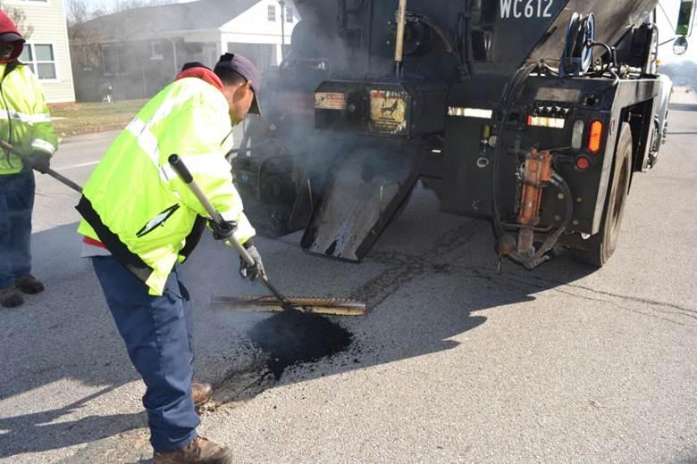 Trabajador de mantenimiento vial limpiando escombros para la reparación de baches.