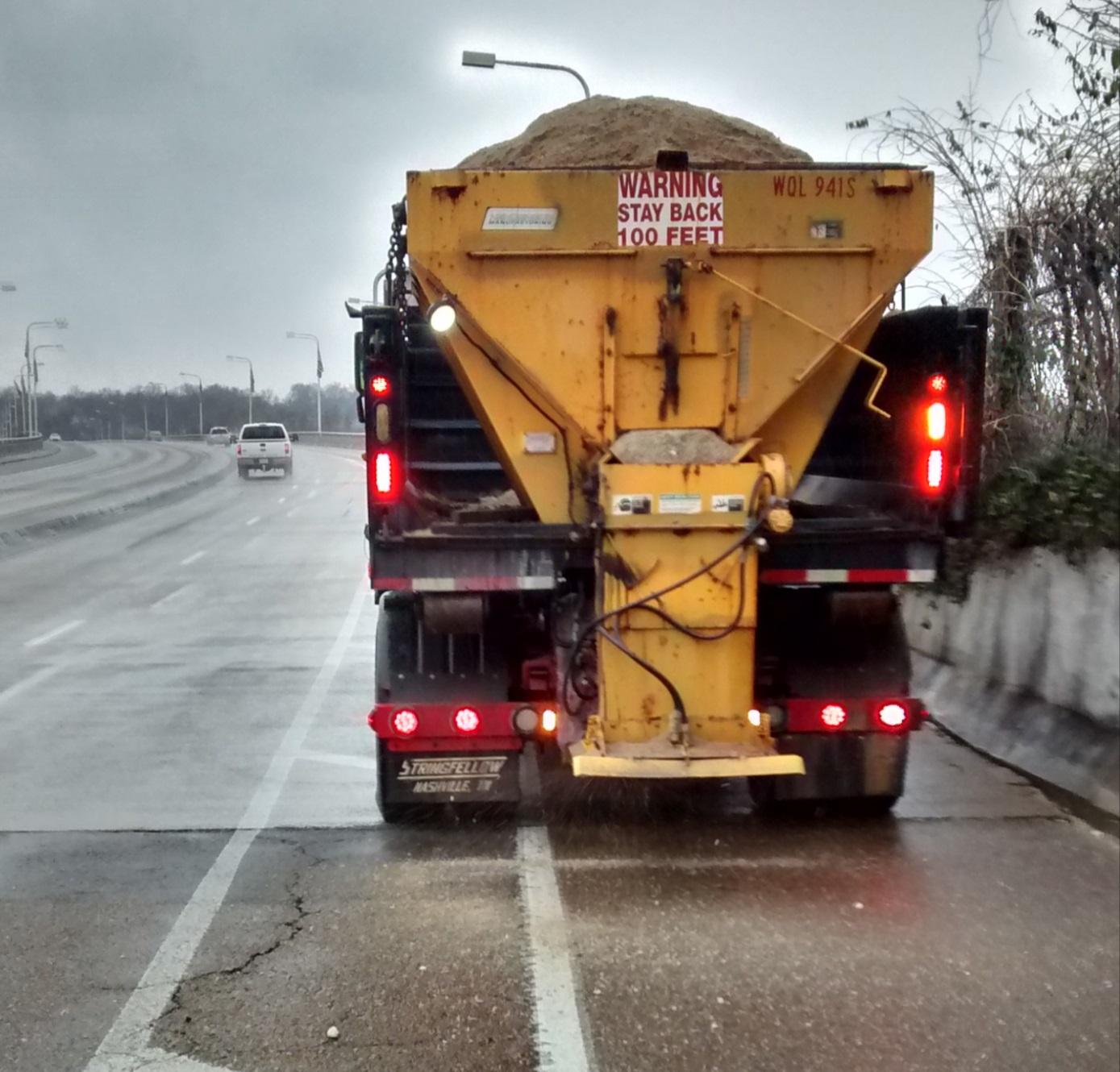 A large truck with a load of ice melting agents parked on the side of the road, undergoing salt treatment.