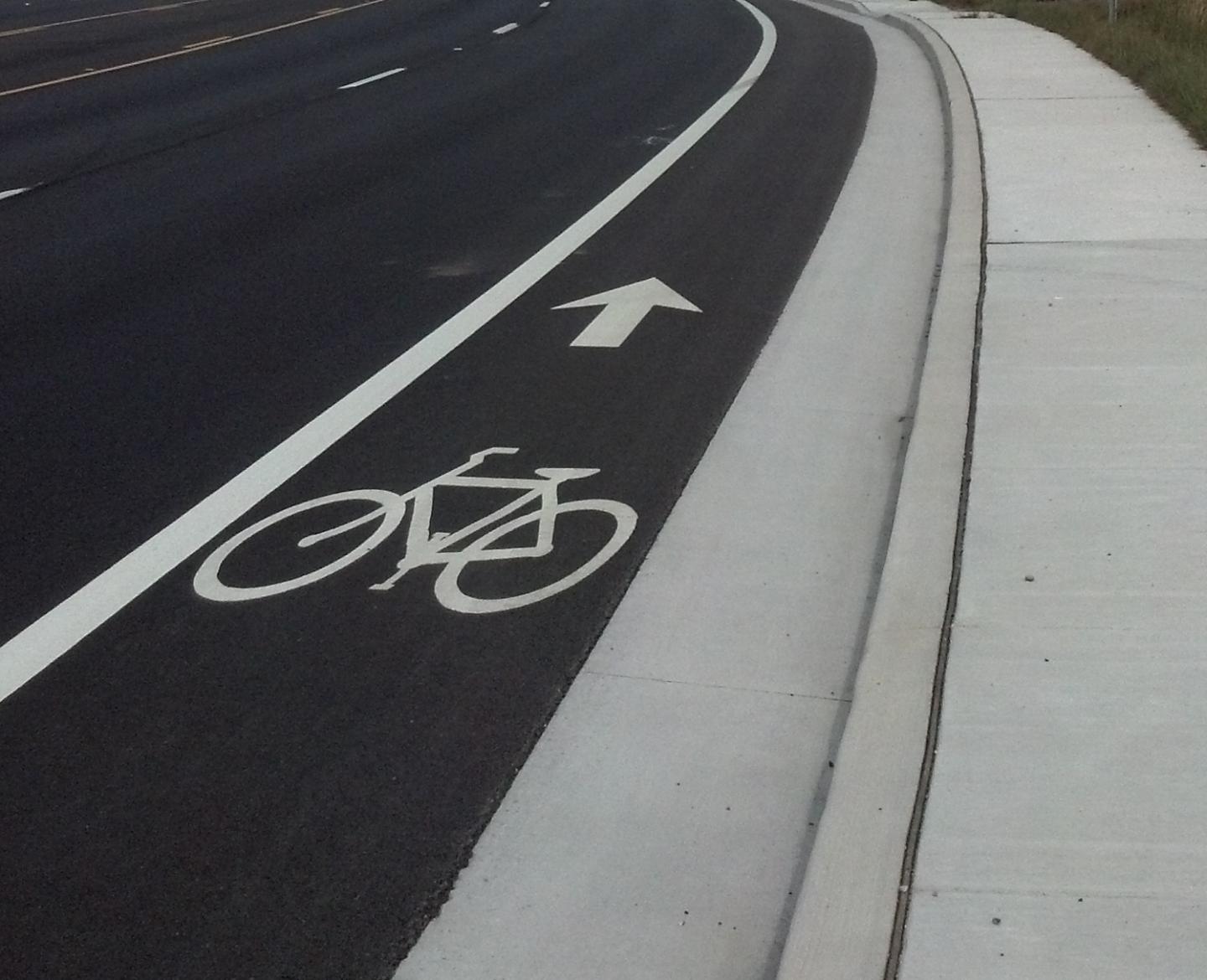 A bike lane on a highway with a white arrow pointing right, indicating the designated path for cyclists.