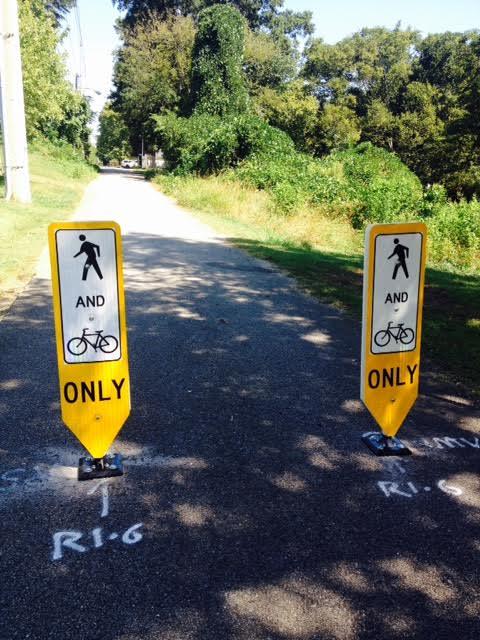 Two signs on a paved road: one says "only" and the other says "bike". Promotes safe, pedestrian-friendly routes for transportation and recreation.