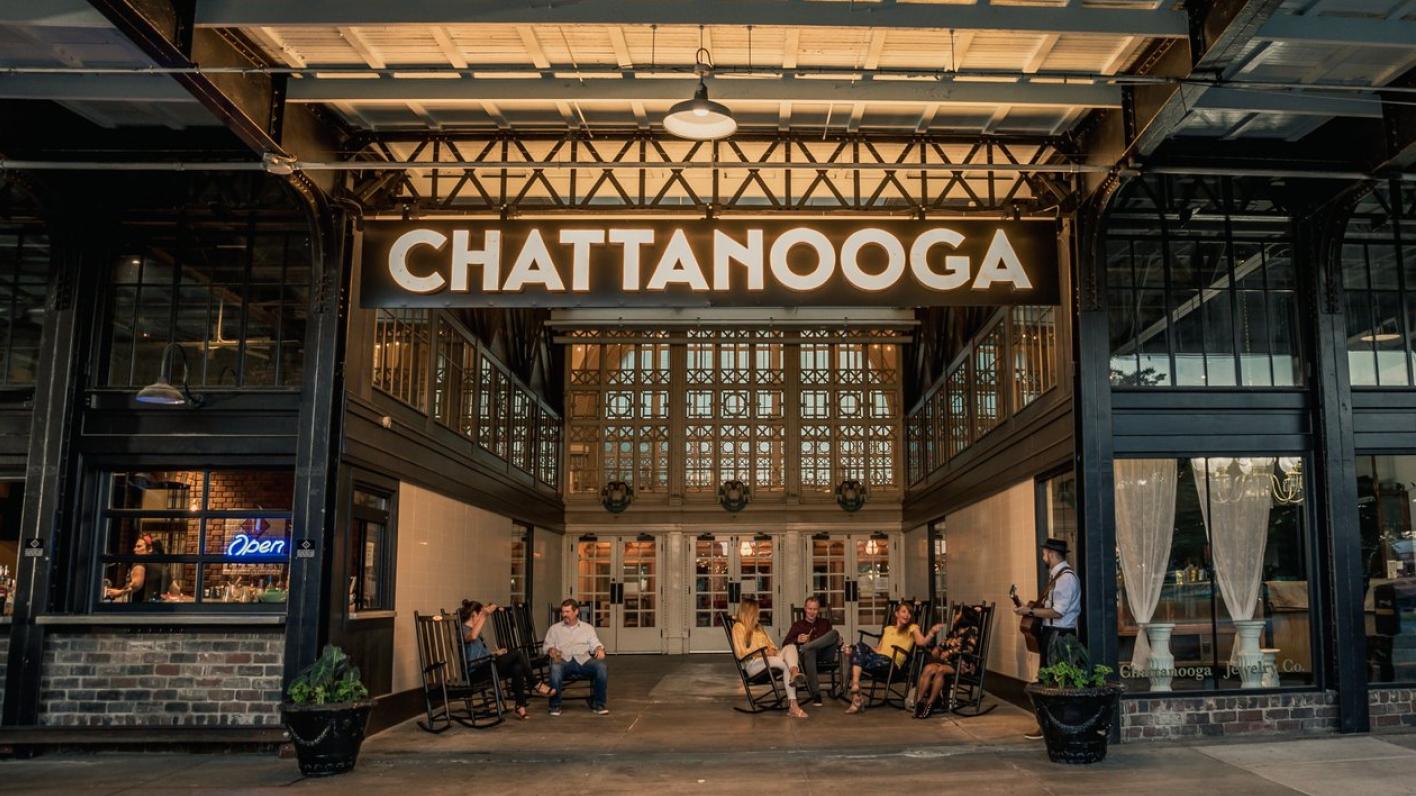 Entrance of a historic building with a large 'Chattanooga' sign, featuring people seated in rocking chairs and socializing.