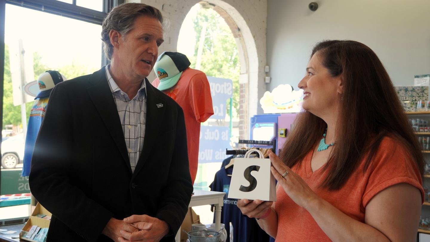 Woman holding a small white bag with a black s talking to Mayor Tim Kelly