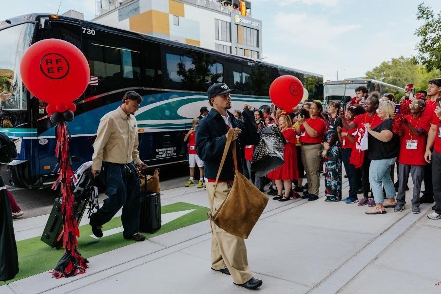 Fans stand next to bus while watching Football team arrive